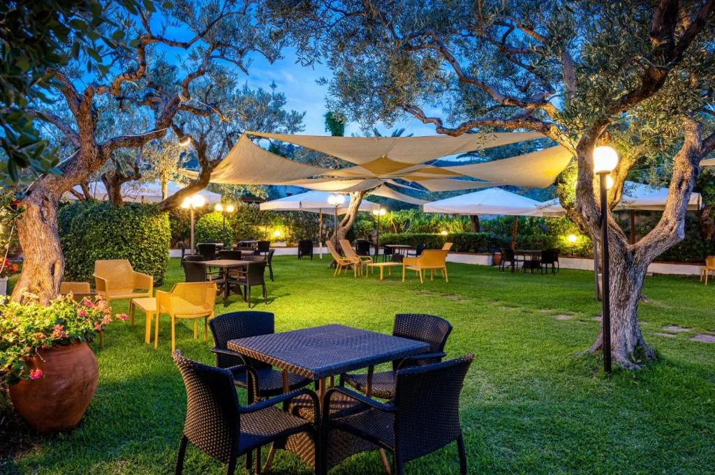 Giardino con tavoli e sedie tra ulivi illuminati di sera
