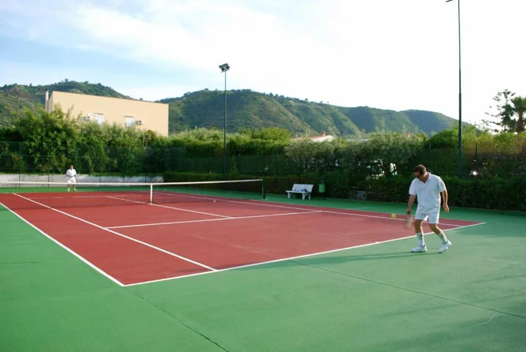 Campo da tennis con giocatori e colline verdi sullo sfondo