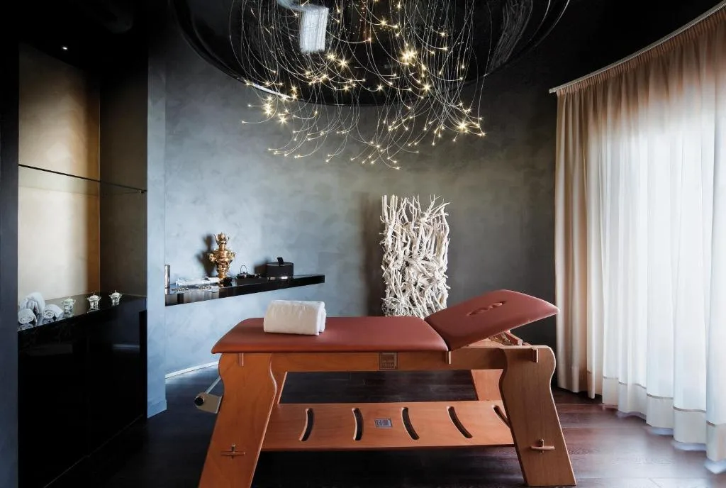 Sala massaggi spa con lettino, pareti scure e lampadario luminoso