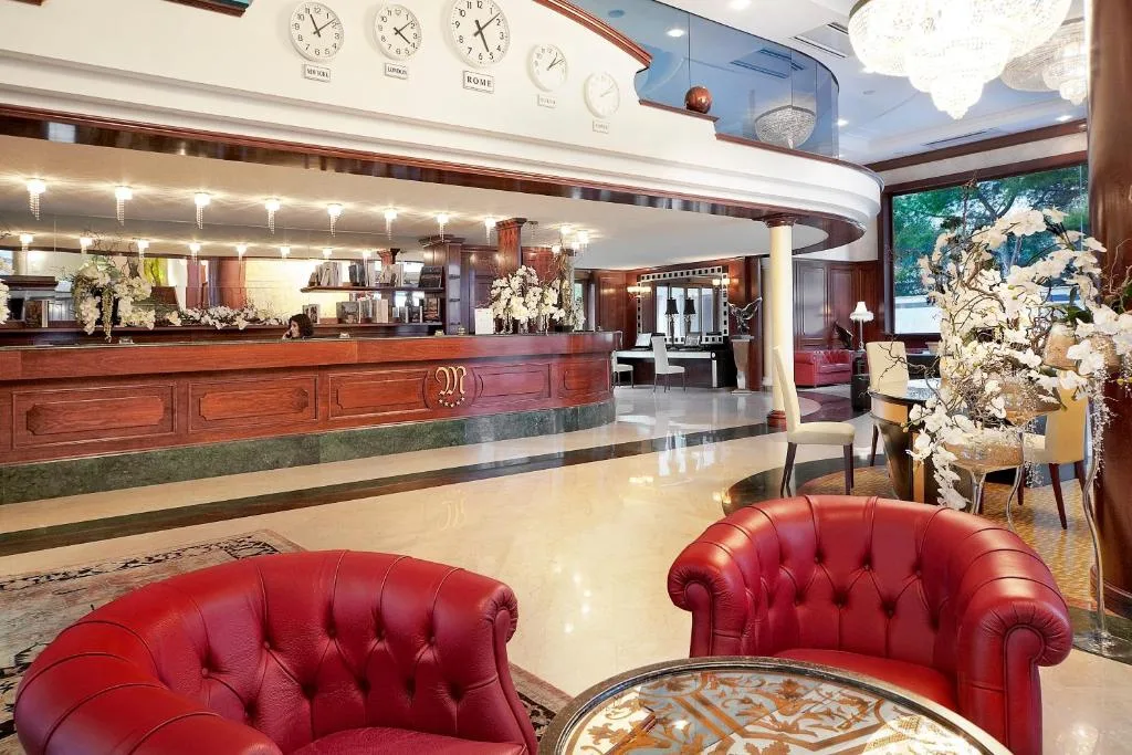 Hall dell'hotel con reception in legno, poltrone in pelle rossa e lampadario di cristallo