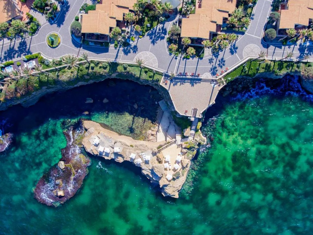 Veduta aerea di solarium roccioso con lettini bianchi sul mare verde smeraldo