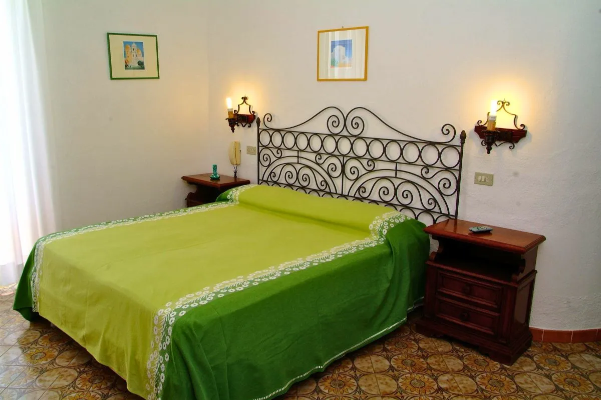 Camera matrimoniale con testiera in ferro battuto, copriletto verde e pavimento in maioliche