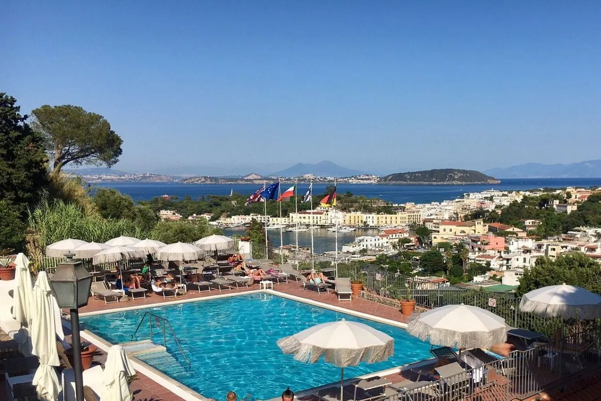 Piscina panoramica con lettini, ombrelloni e bandiere affacciata sul porto e sul golfo di Ischia