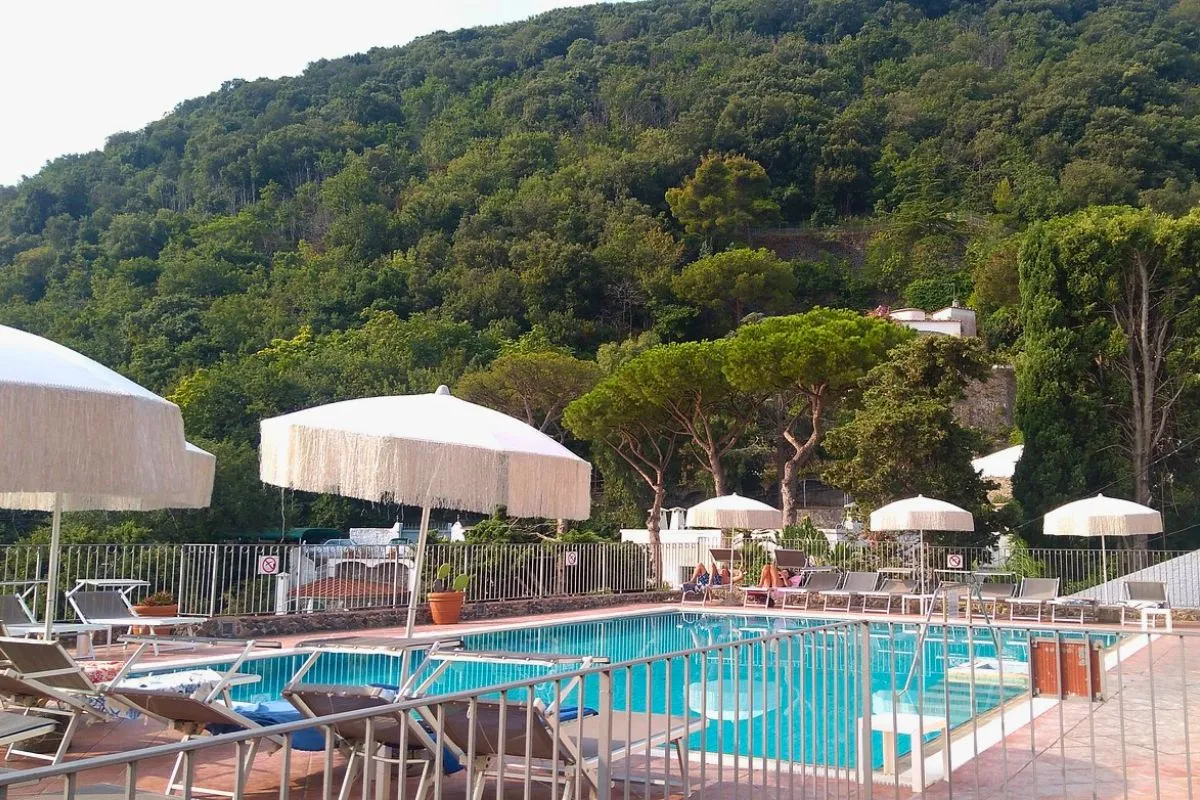 Piscina circondata da lettini e ombrelloni bianchi immersa nel verde della collina boscosa