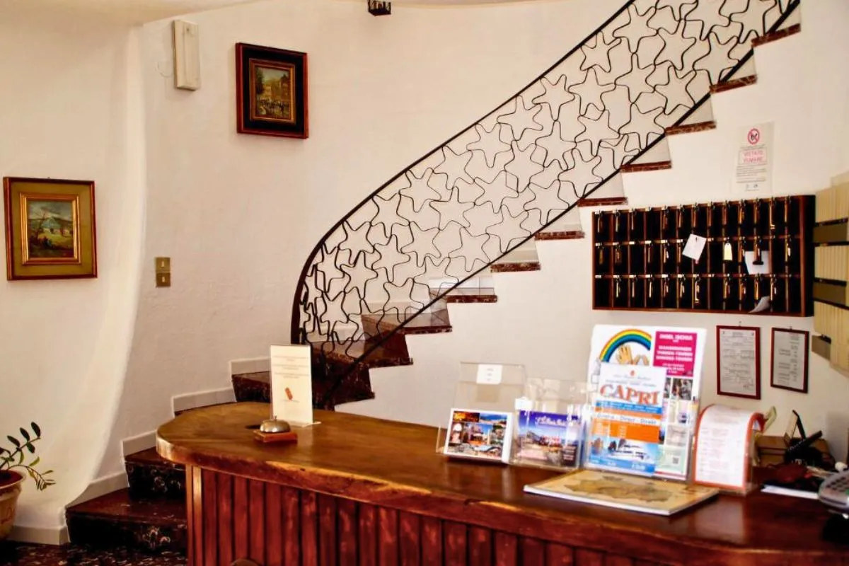 Reception dell'hotel con bancone in legno, scala elicoidale e quadri alle pareti