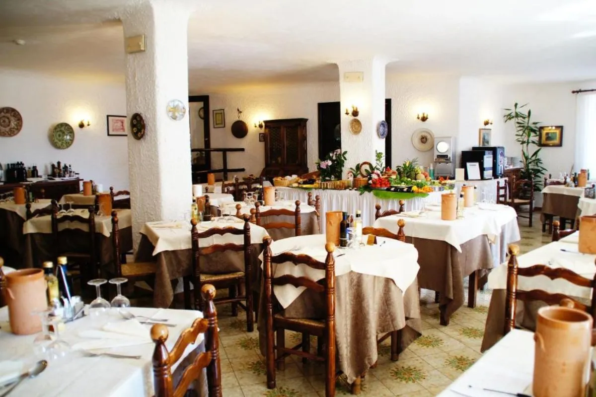 Sala ristorante con tavoli apparecchiati, sedie in legno e buffet di frutta e verdura al centro