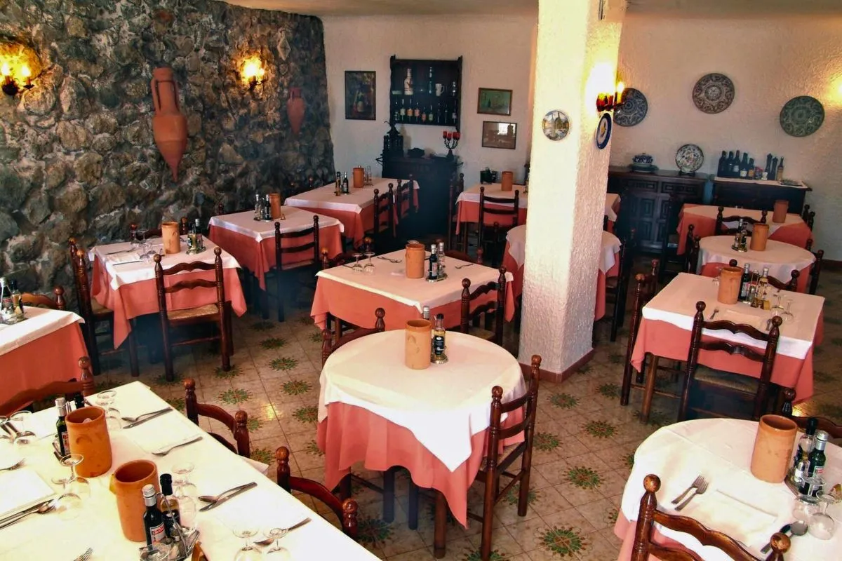 Sala ristorante rustica con tavoli apparecchiati, tovaglie rosa e parete in pietra