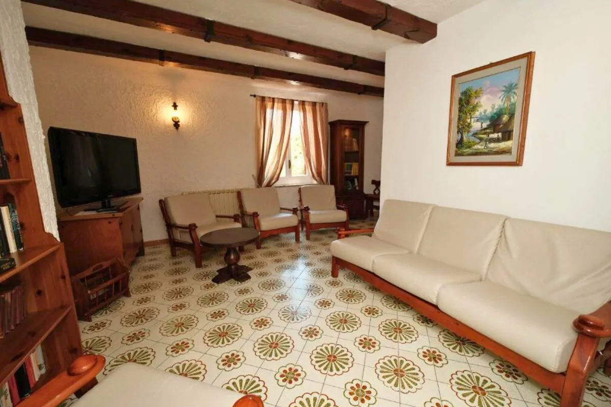 Salotto con divani bianchi, televisore, travi a vista e pavimento in piastrelle decorate