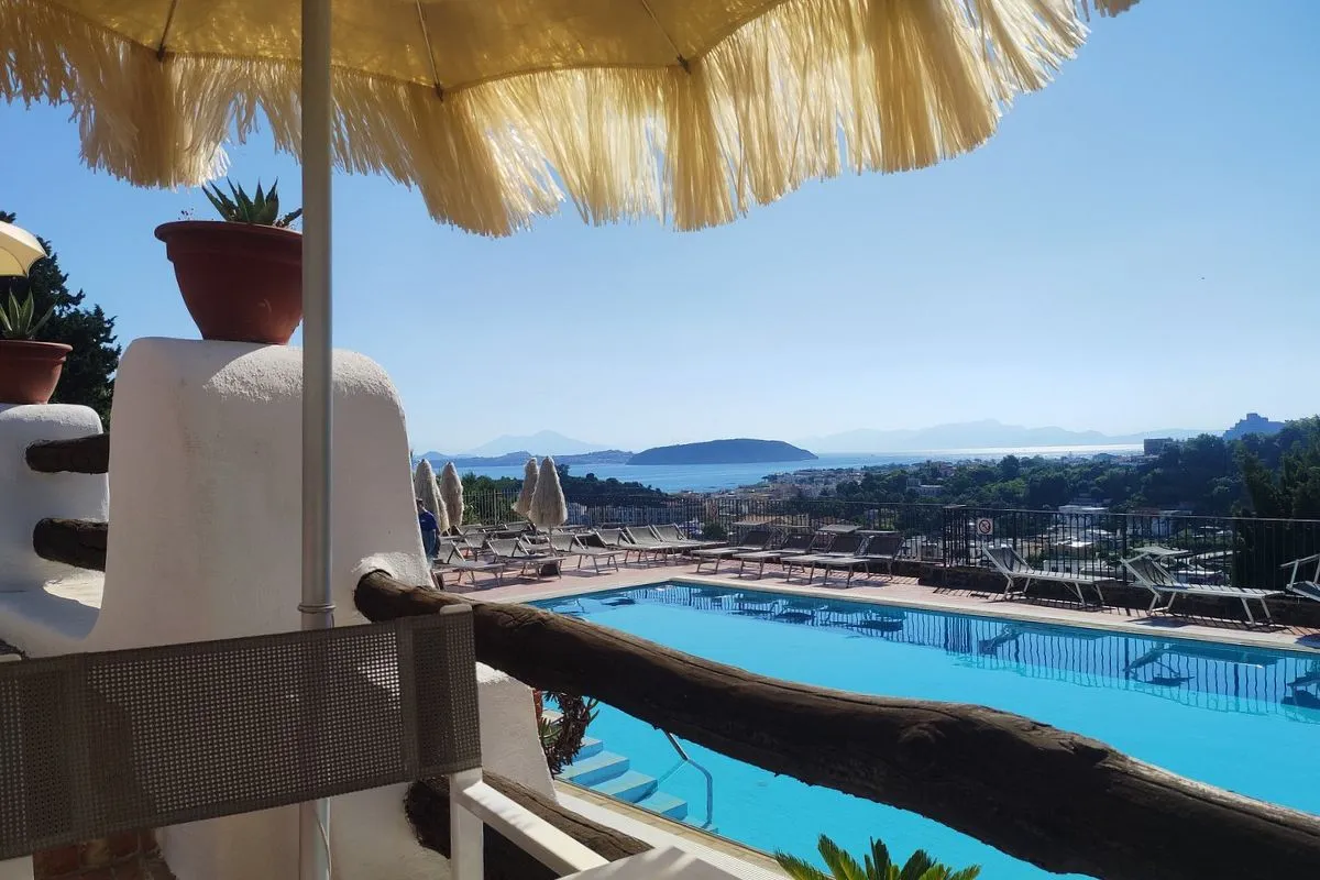 Vista sulla piscina e sul golfo da una terrazza ombreggiata con ombrellone in paglia