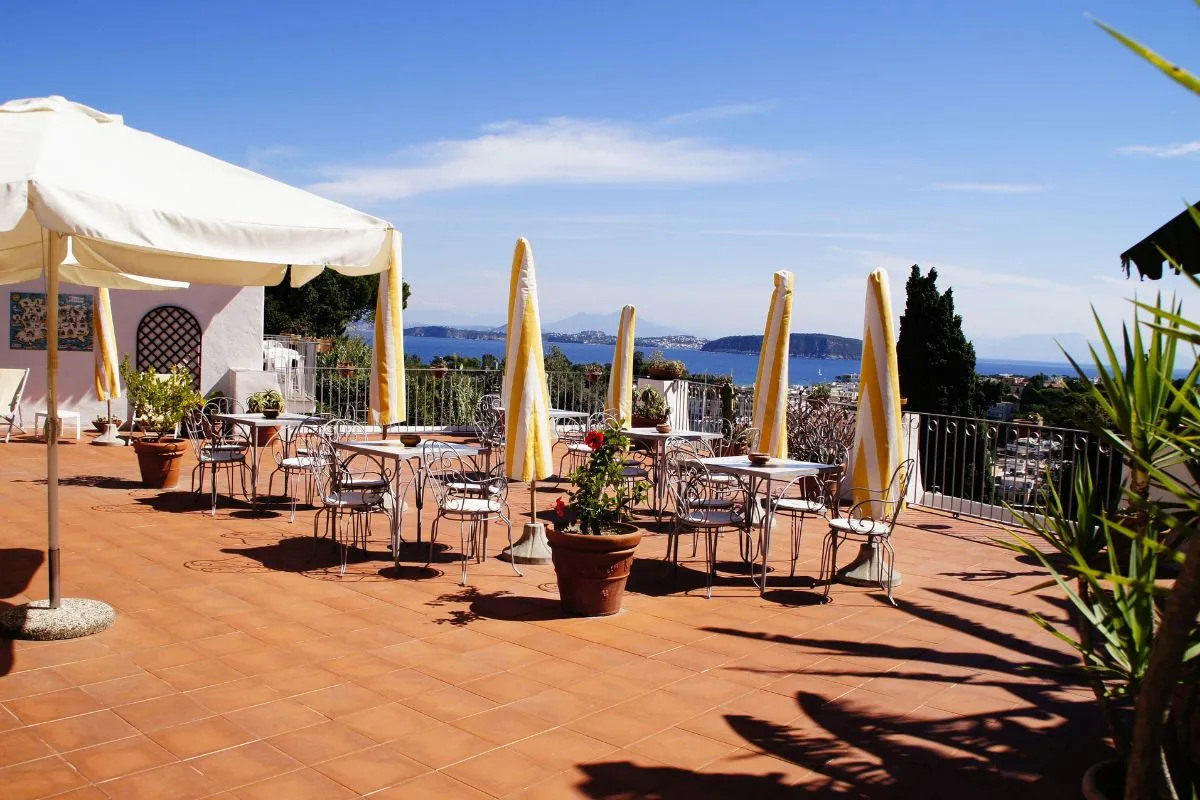 Terrazza solarium con tavoli, sedie in ferro battuto e ombrelloni gialli affacciata sul mare