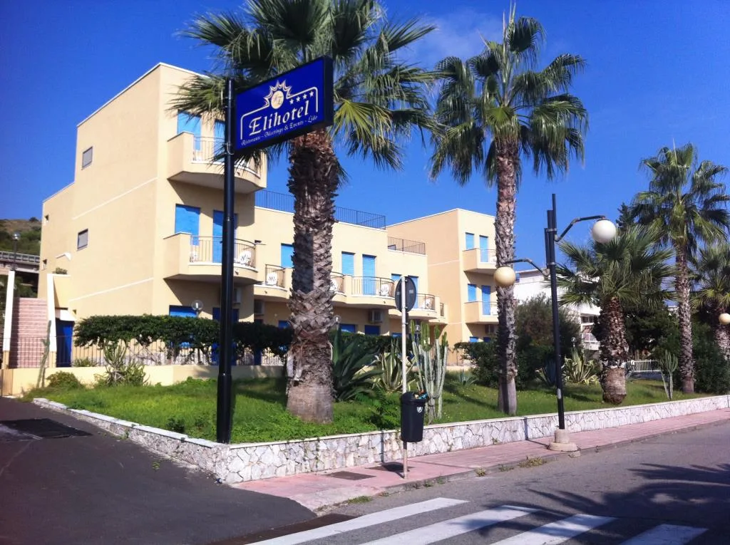 Esterno dell'Elihotel con palme, giardino e insegna dell'albergo