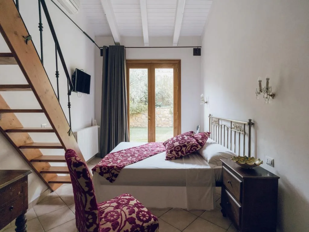 Camera con letto in ferro battuto, scala in legno e portafinestra sul giardino