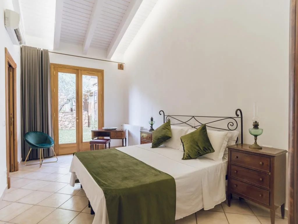 Camera luminosa con letto matrimoniale, dettagli verdi e portafinestra sul giardino