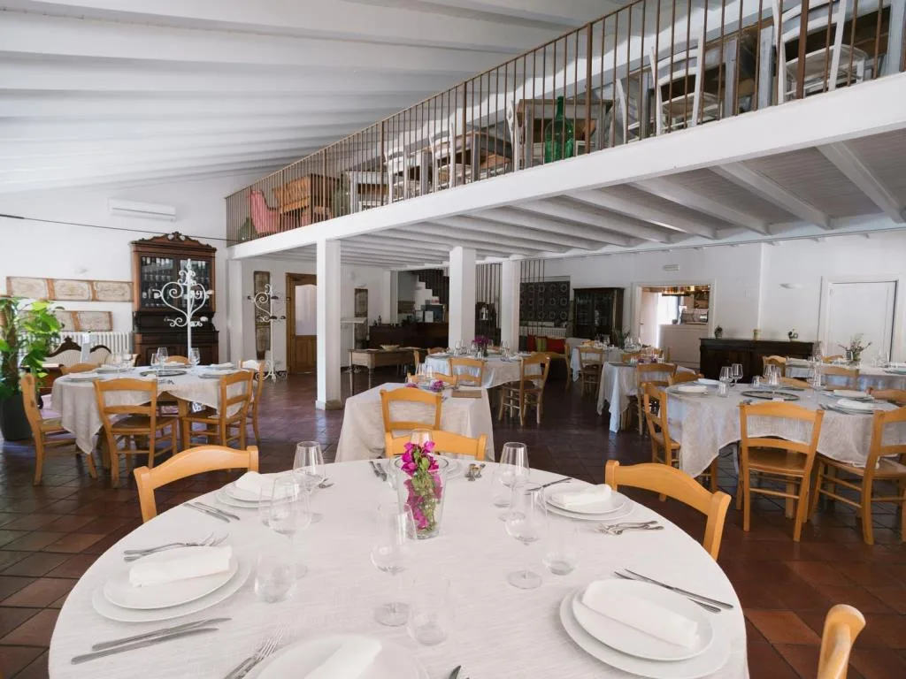 Sala ristorante interna con tavoli apparecchiati, soppalco e travi bianche