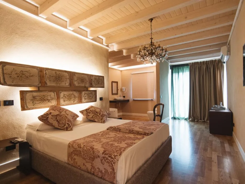 Ampia camera matrimoniale con travi in legno, lampadario e testiera decorata