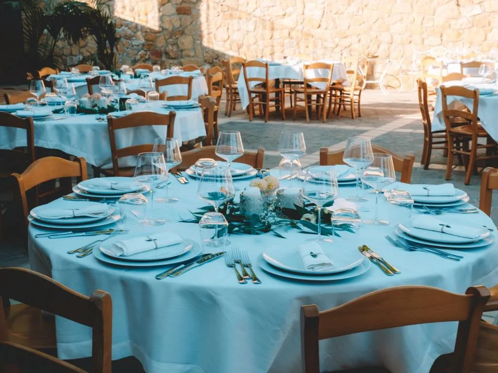 Tavolo rotondo apparecchiato con tovaglia bianca e calici per un evento all'aperto