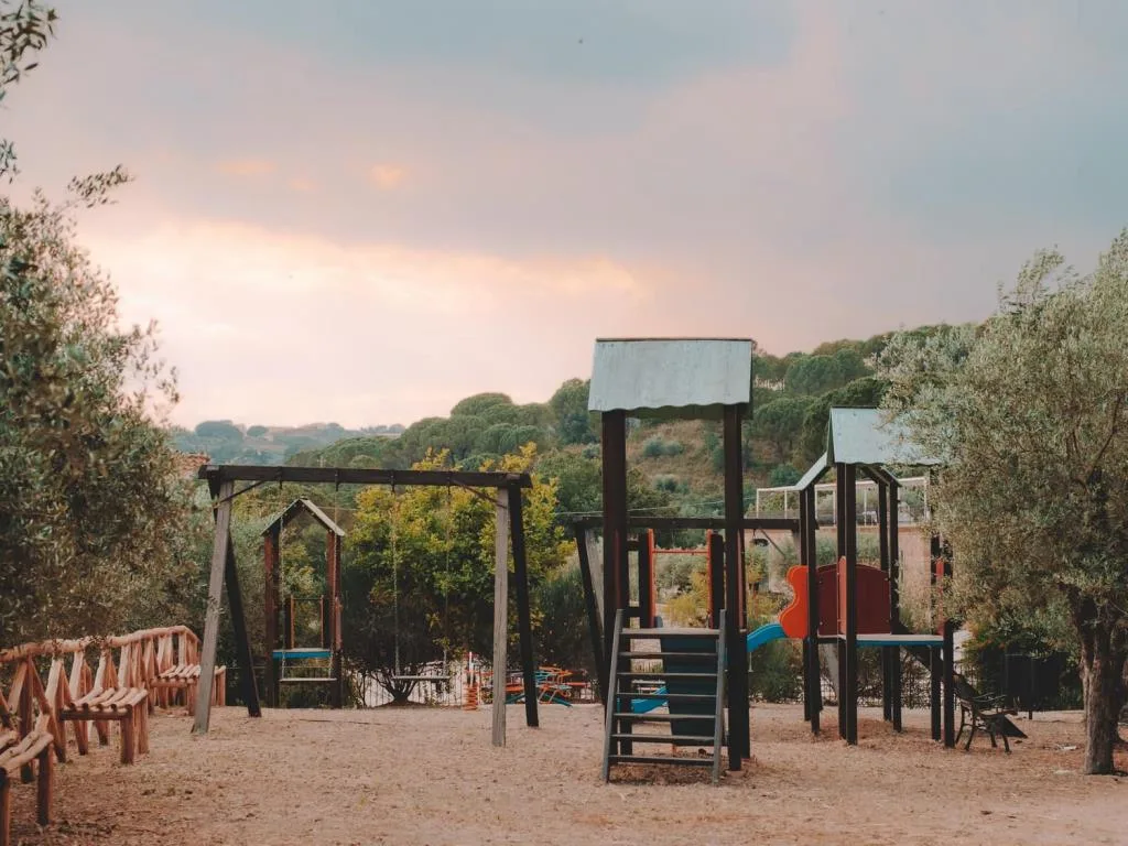 Area giochi per bambini con altalene e scivoli tra gli ulivi al tramonto