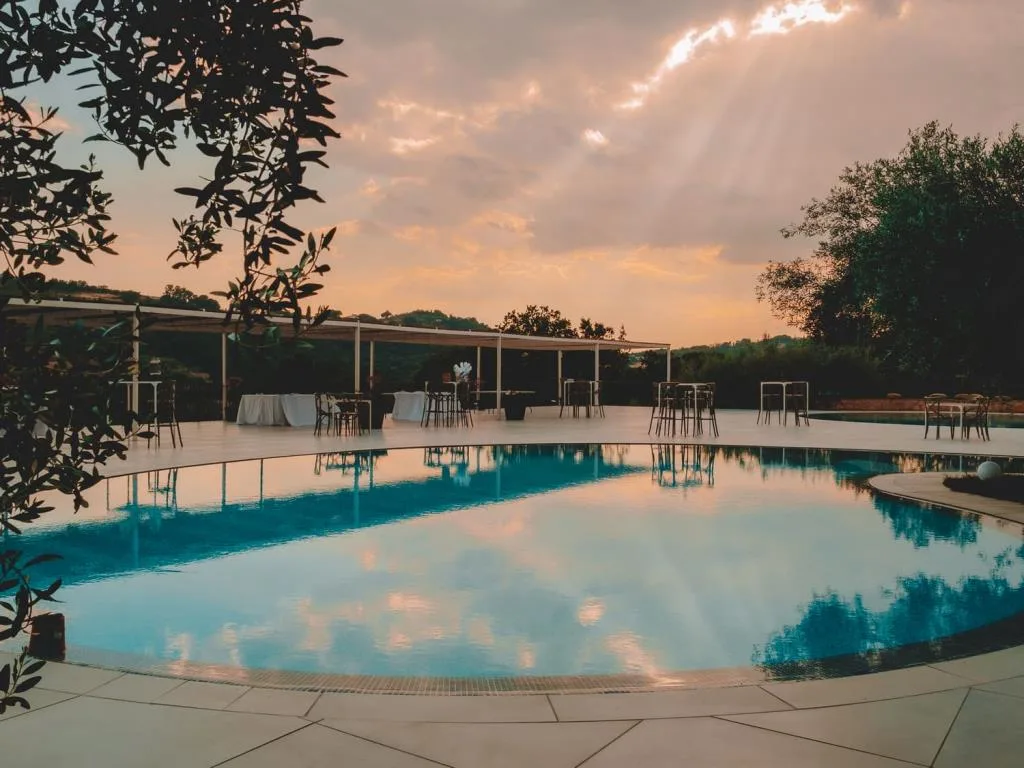 Piscina al tramonto con area lounge e tavoli sotto una pergola