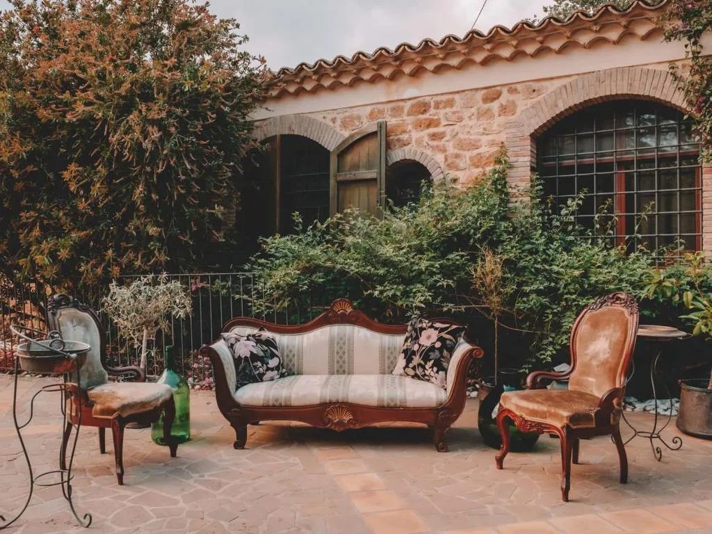 Patio in pietra con divano e poltrone antiche circondato da vegetazione