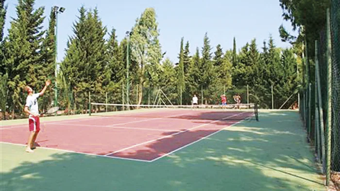 Campo da tennis in terra rossa immerso nel verde con persone che giocano