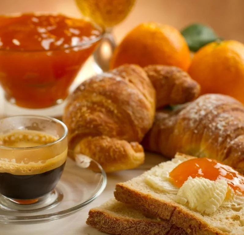 Colazione italiana con caffè espresso, cornetti, marmellata di arance e pane con burro