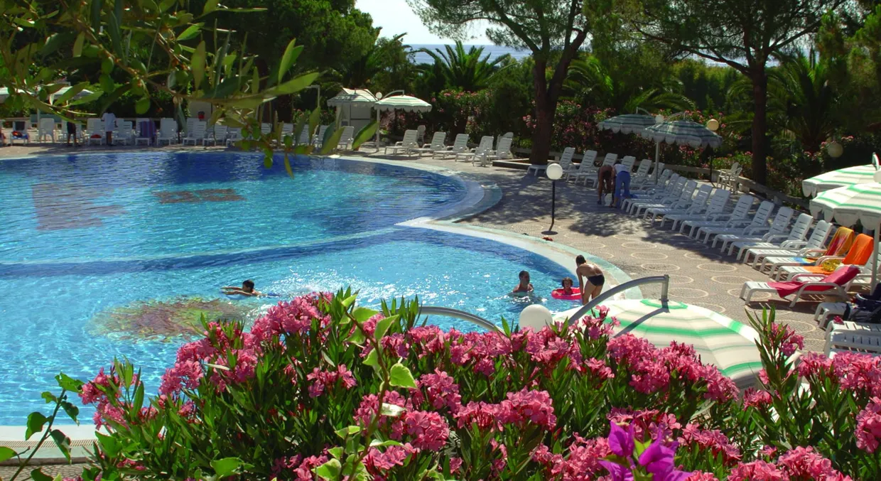 Piscina con bagnanti circondata da fiori rosa e vegetazione