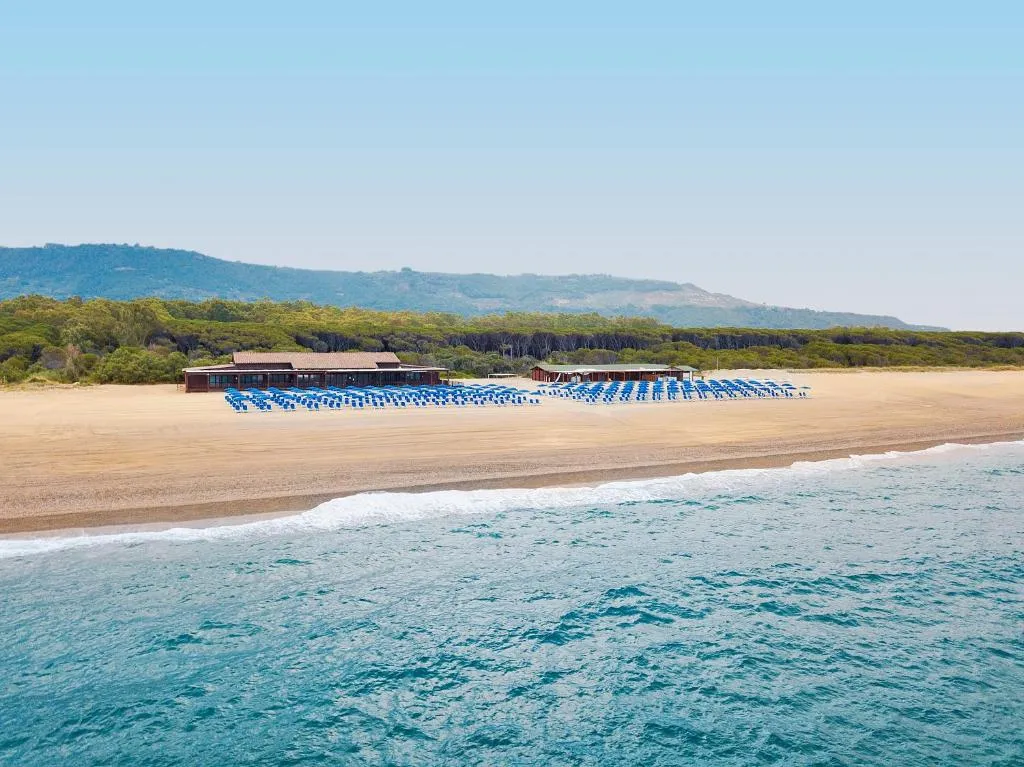 Spiaggia attrezzata con file di lettini blu, mare e colline sullo sfondo