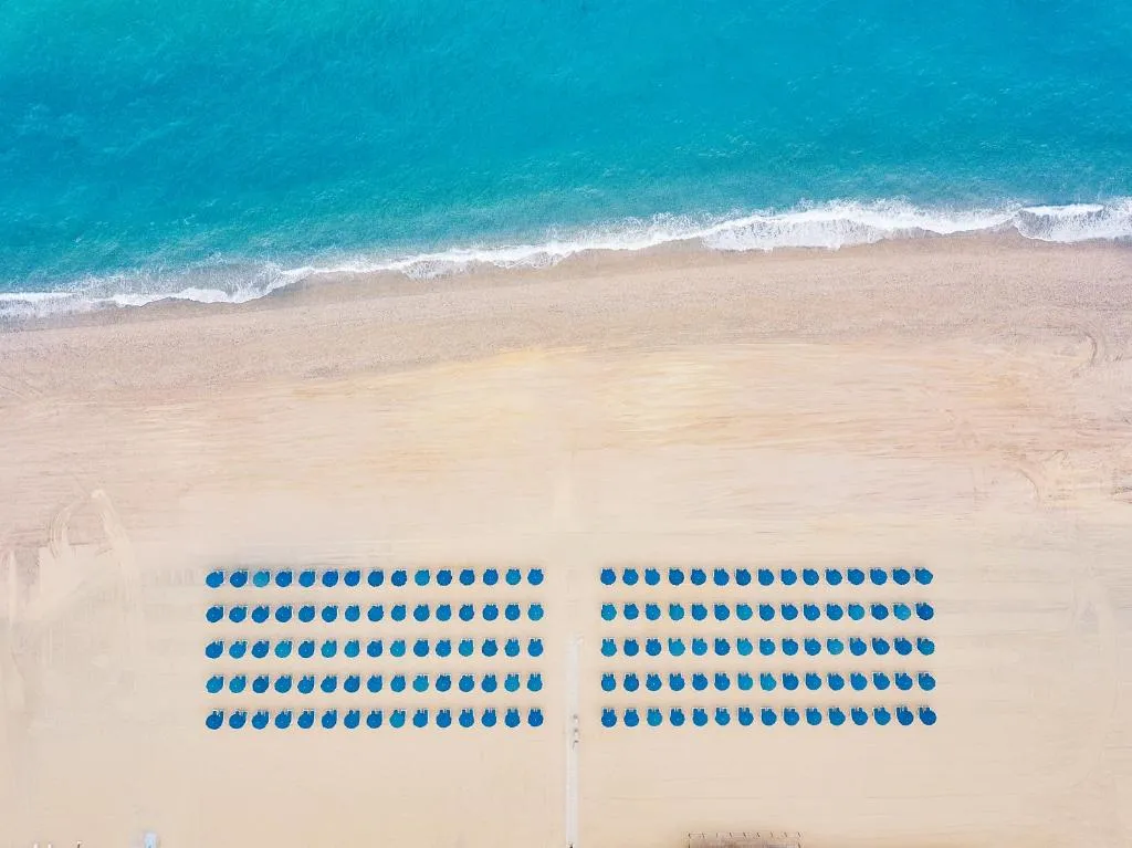 Veduta dall'alto della spiaggia con ombrelloni blu disposti in file e mare turchese