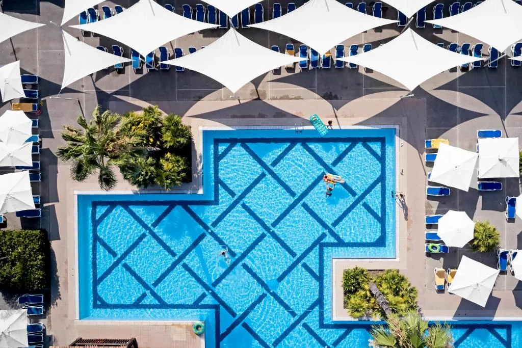Piscina con disegni geometrici blu, vele ombreggianti bianche e lettini visti dall'alto