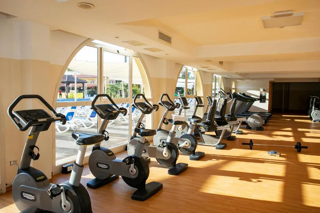 Sala fitness con cyclette, tapis roulant e grandi finestre affacciate sulla piscina