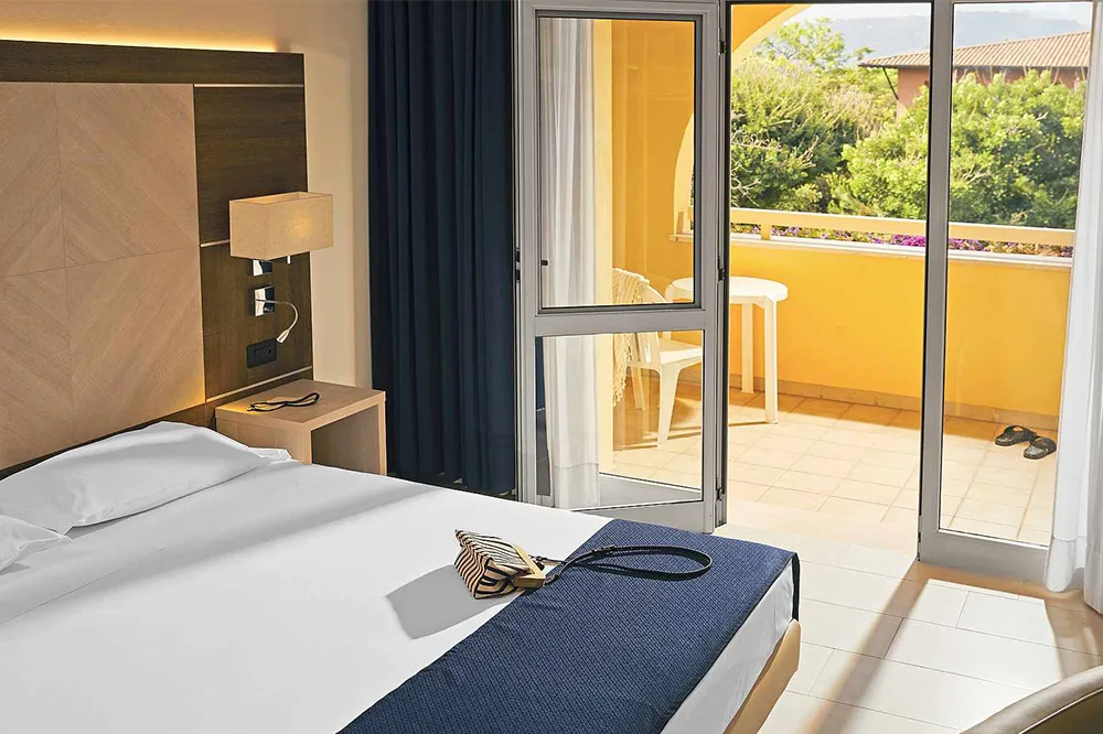 Camera matrimoniale luminosa con letto bianco e balcone vista vegetazione