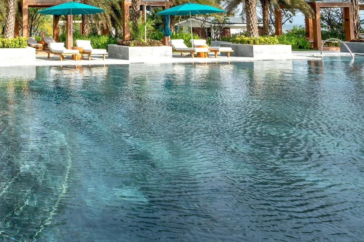 Piscina con acqua limpida, lettini bianchi e ombrelloni turchesi tra le palme
