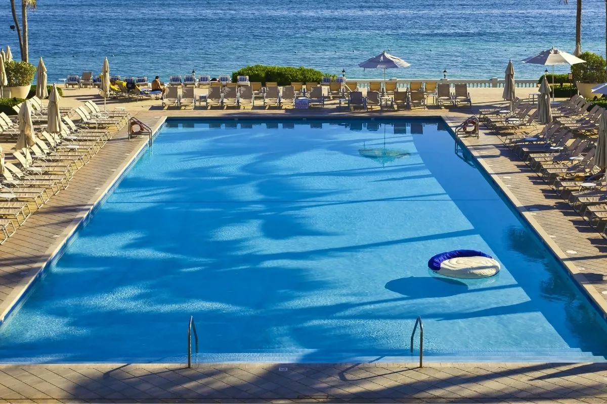 Grande piscina rettangolare con lettini e ombrelloni affacciata sul mare