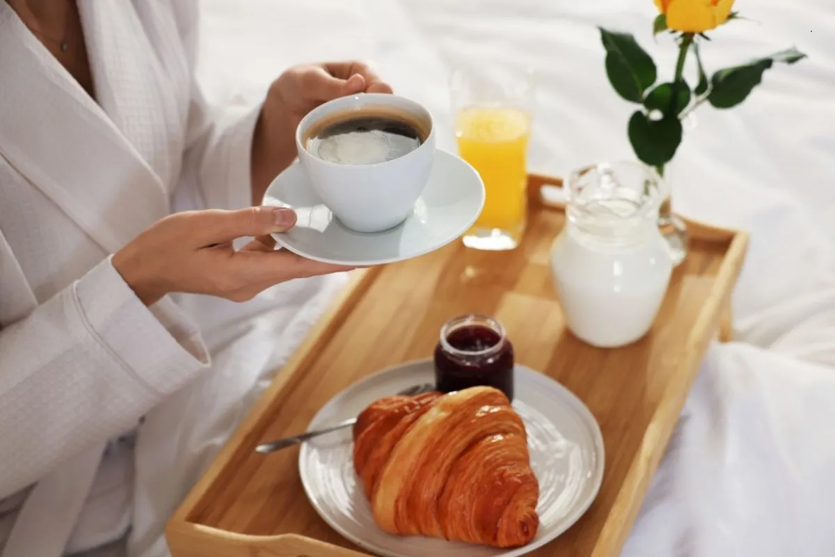 Colazione a letto servita su vassoio di legno con caffè, cornetto e succo d'arancia