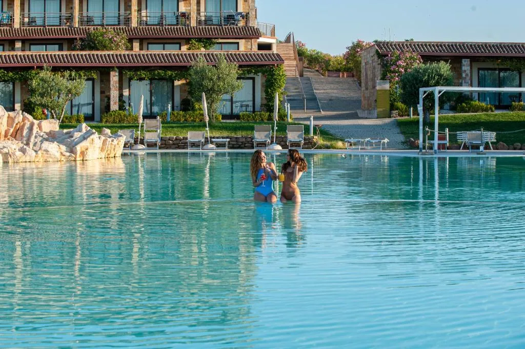 Due donne in bikini con cocktail nella piscina davanti all'edificio del resort