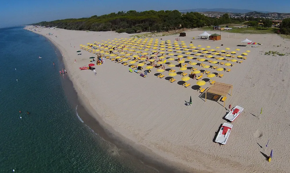 Spiaggia di sabbia con ombrelloni gialli e pedalò lungo la riva del mare