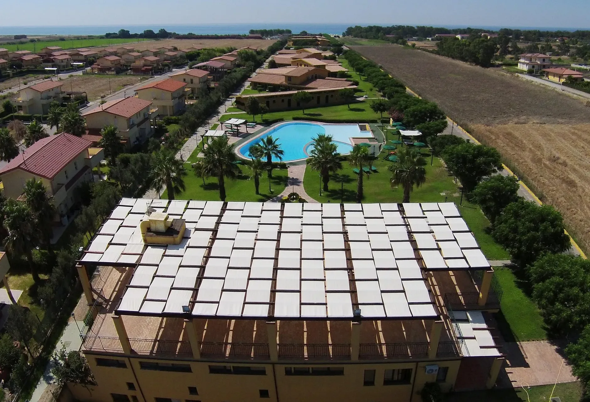 Vista aerea del resort con piscina, giardino con palme e villette con vista mare