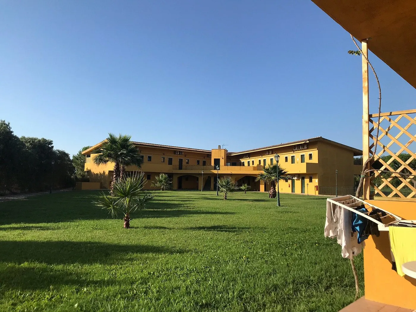 Vista del cortile interno con prato verde, palme e edifici gialli dell'hotel