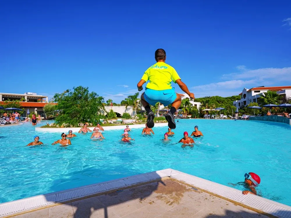 Animatore che salta in piscina durante attività di acquagym con ospiti