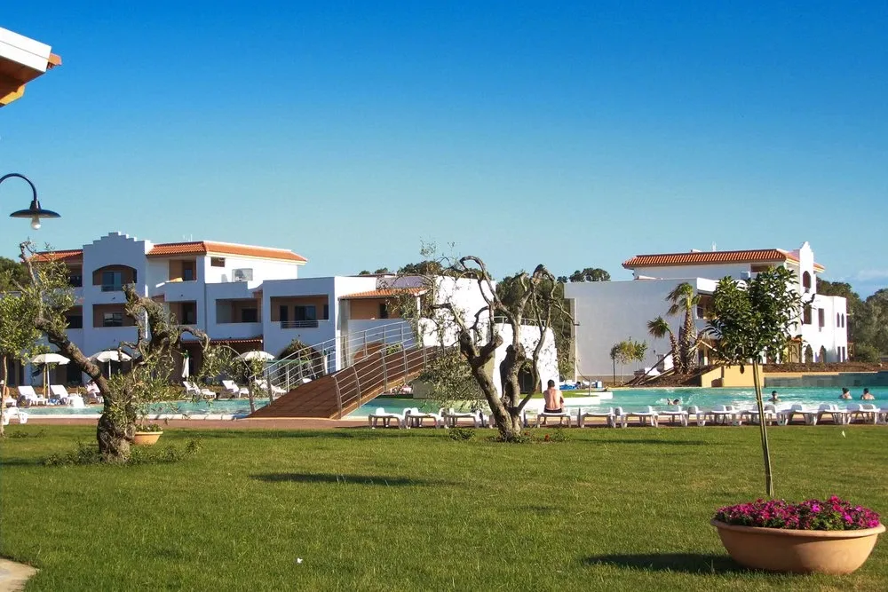 Giardino verde con ulivi e piscina sullo sfondo degli edifici del resort