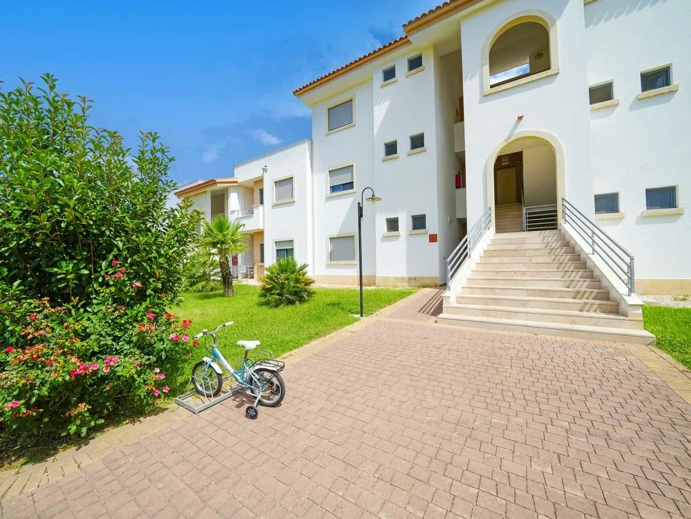 Esterno di edificio bianco del resort con giardino fiorito e bicicletta per bambini
