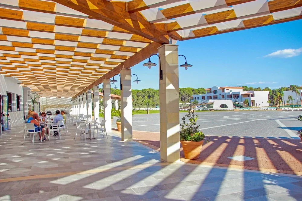 Terrazza coperta con pergolato in legno, tavoli e vista sul resort