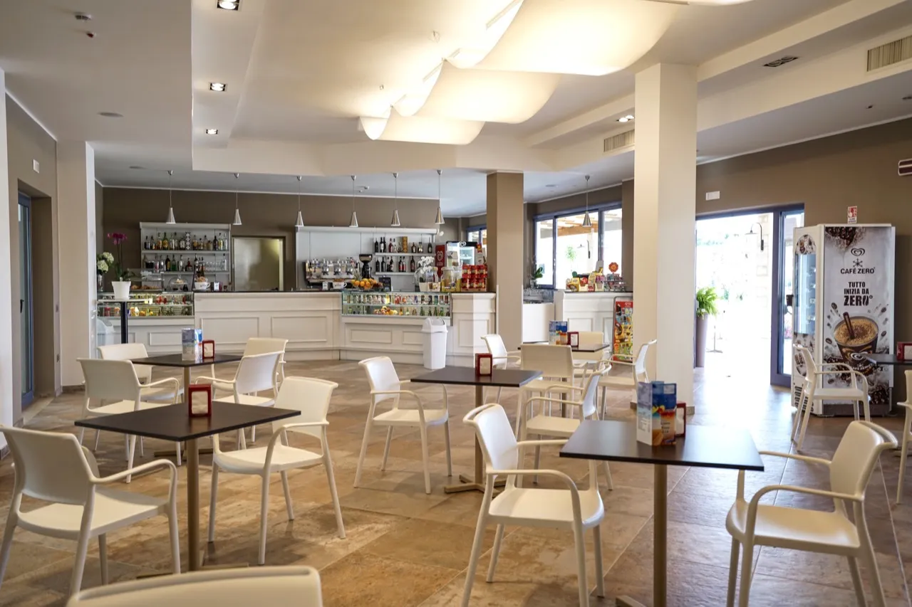 Interno del bar del resort con bancone, tavoli e sedie bianche