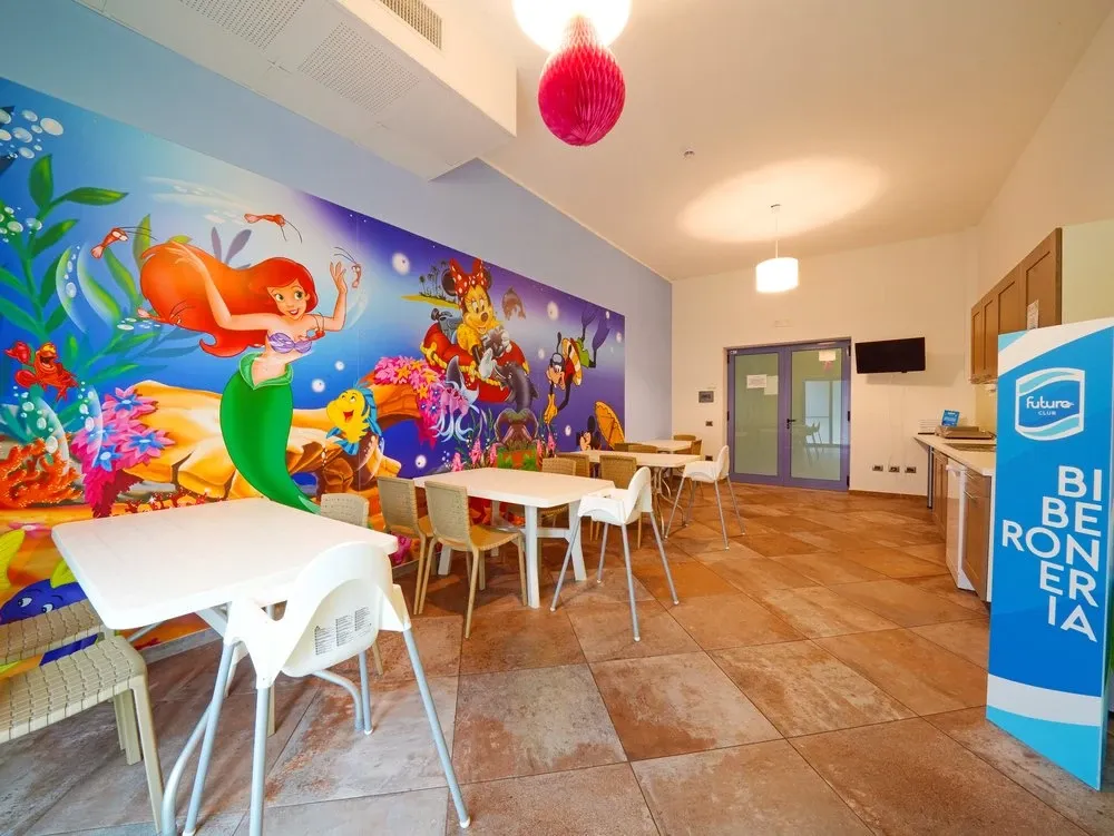Sala biberoneria per bambini con murale colorato e tavolini