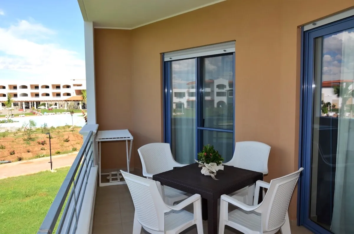 Balcone con tavolo, sedie bianche e vista sul giardino e piscina