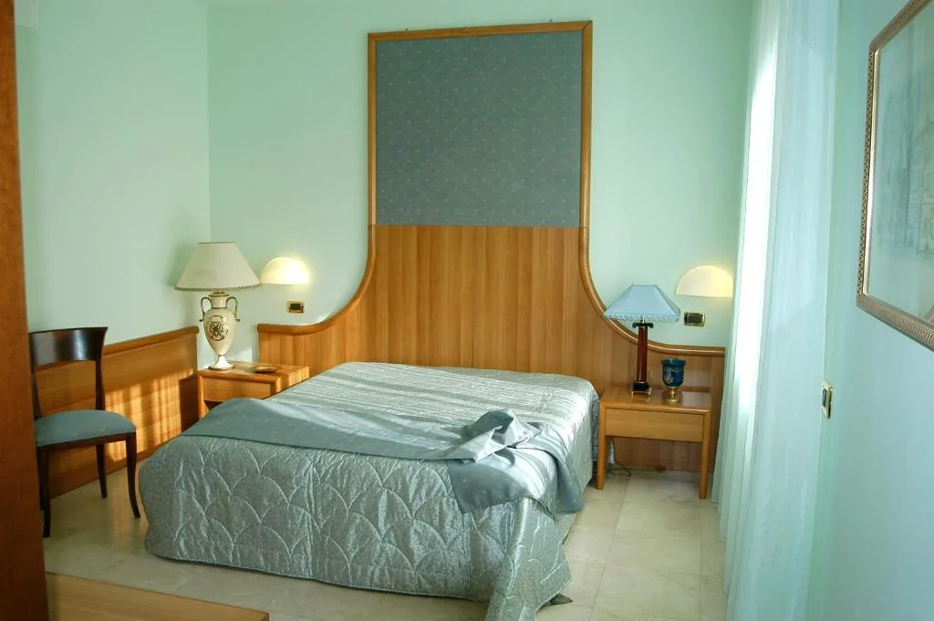 Camera con letto matrimoniale, testiera in legno, comodini e lampade abat-jour
