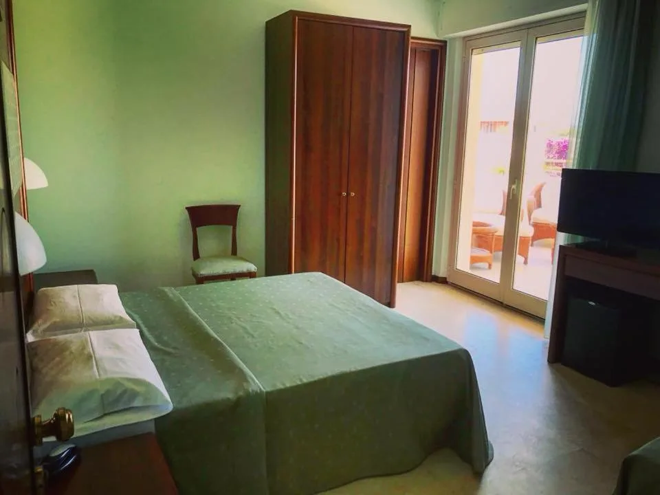 Camera con pareti verdi, letto matrimoniale, armadio in legno e accesso al balcone