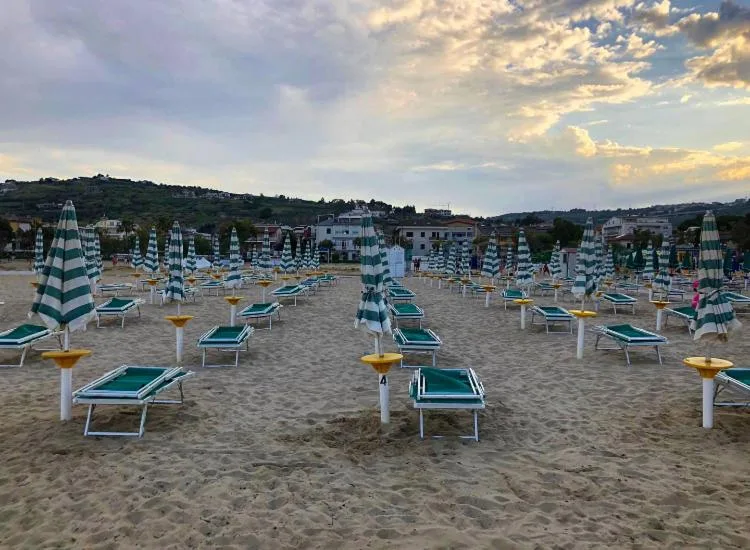Spiaggia attrezzata con ombrelloni chiusi e lettini con vista sulle colline