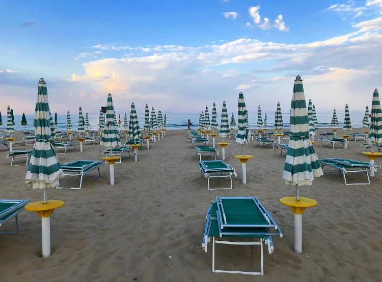 Spiaggia con ombrelloni a righe verdi e lettini vista mare al tramonto