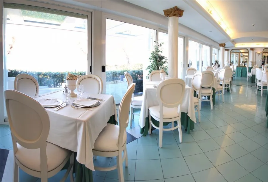 Sala ristorante luminosa con tavoli bianchi apparecchiati, colonna decorata e ampie vetrate